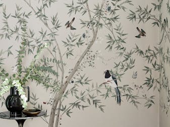 Bedroom featuring blue wallpaper with a vibrant peacock print (Pavona – Sylvie), behind a bed with a green velvet headboard.