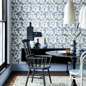 Dining space with white and blue floral wallpaper, powder blue skirting boards and a black table and chair.