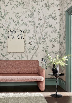 Living room with an off-white bird print mural wallpaper (Belton Scenic - Oyster) with a pink sofa and small table.