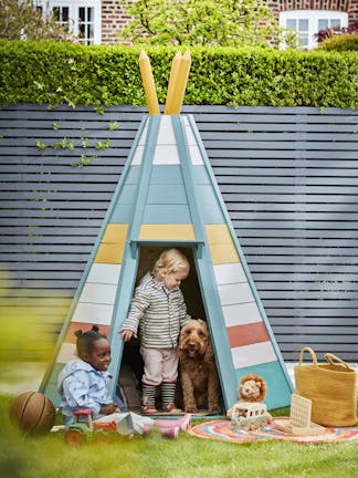 Multi colored tee-pee in a back yard in front of a paneled fence in dark blue (Juniper Ash) with two children and a dog playing.