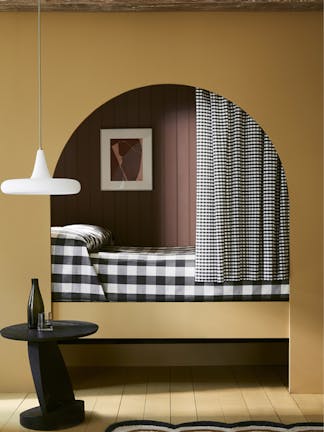 Bedroom with yellow painted arch (Bassoon) leading to a gingham bed with curtain.