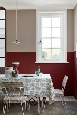 Dining room with upper wall in warm neutral 'Rolling Fog - Dark' and lower wall in deep red 'Arras', with a table and chairs.