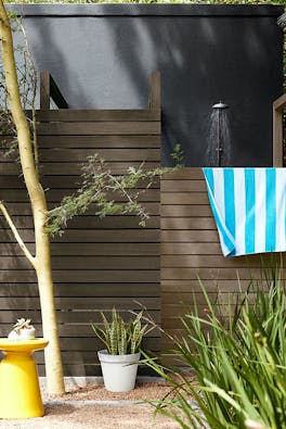 Outside shower area with a paneled fence with a rich black wall (Lamp Black), surrounded by plants.