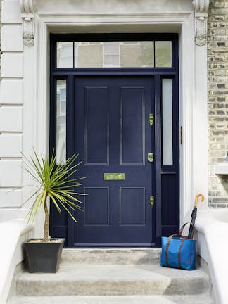 A luxury black-blue door painted in 'Balsat' with a large plant to the left and a blue bag holding an umbrella to the right.