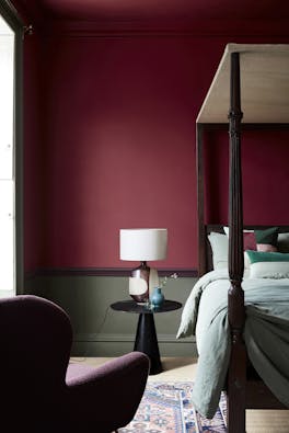 Deep red (Baked Cherry) bedroom with a contrasting dark green lower wall behind a four poster bed and armchair.