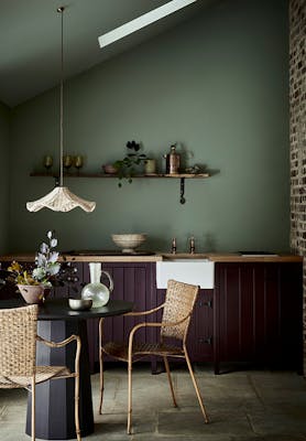 Kitchen with a soft green back wall (Windmill Lane) and aubergine purple (Cordoba) kitchen cabinets with a table and chairs.