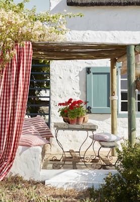 Yard with exerior wall in off white Wood Ash and pale blue shutters (Celestial Blue) with a seating area surrounded by trees.