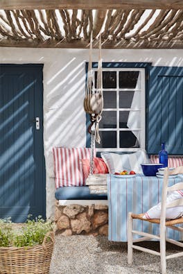 Yard with door and shutters painted in deep blue (Hicks' Blue) and a white wall, with a seating area and striped cushions.