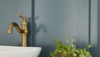 Close up of a white basin with a gold tap in front of a blue wall painted in 'Etruria'.