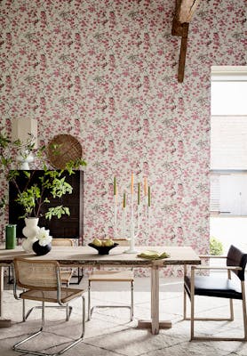 Dining room with pink printed floral and bird wallpaper (Massingberd Blossom - Mineral) and wooden dining table and chairs.