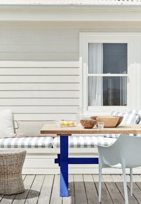 Outdoor dining area with off white paneled wall (Linen Wash) with a striped cushioned chair and wooden table.