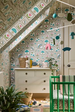 Nursery featuring neutral photo frame print wallpaper (Balance - Portland Stone) with a dresser, green crib and a plant.