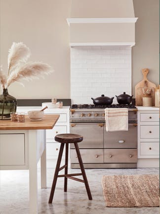 Neutral kitchen with beige walls, white tiling, silver appliances, white cabinets and a kitchen island with wooden top.