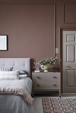 Bedroom painted in warm red (Nether Red) with contrasting grey woodwork and a bed scattered with cushions.