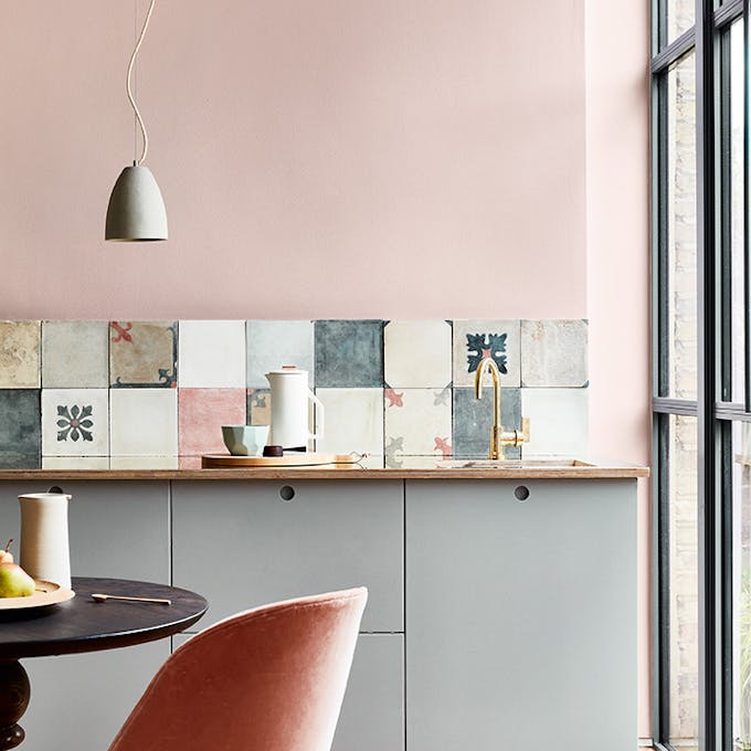 Kitchen with Light Peachblossom wall, colorful backsplach, blue cabinets and a black table and pink chair.