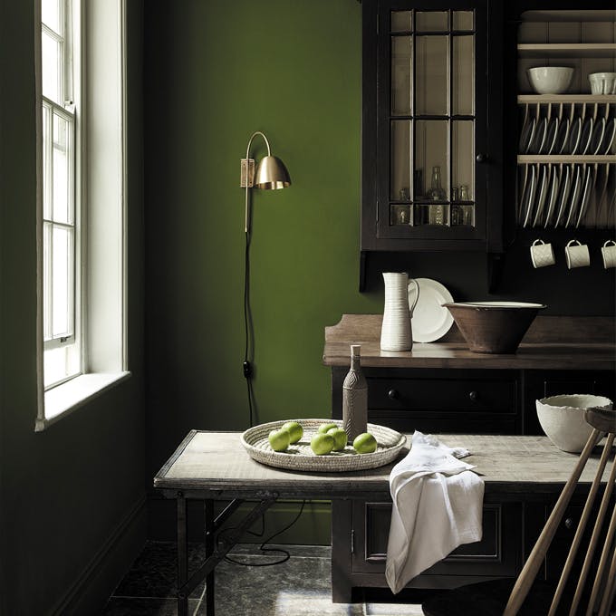 Dining area in deep green shade 'Jewel Beetle' with a wooden table and a rich brown 'Chocolate Color' dresser. 