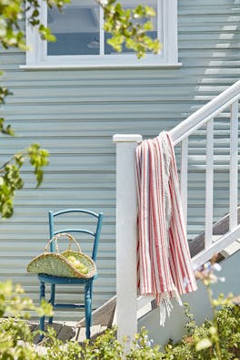 Outdoor cladded wall painted in grey blue shade 'Celestial Blue' with a bright blue chair at the bottom of some outside steps.