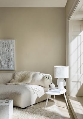 Living room in 3 different neutral shades (Silent White) with a sofa, table and lamp next to a window.