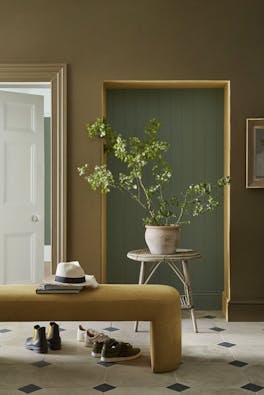 Hallway painted in earthy green shade 'Light Bronze Green' with the alcove in muted green 'Ambleside' next to a gold velvet bench.