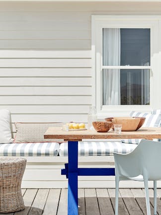 Outdoor dining area with off white paneled wall (Linen Wash) with a striped cushioned chair and wooden table.