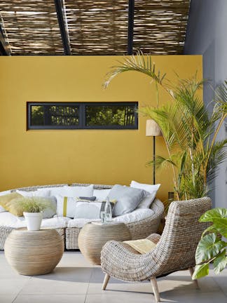 Outside seating area with a large cushioned wicker sofa and chair with a bright yellow wall (Yellow-Pink).