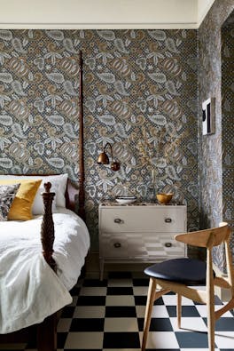 Bedroom with a paisley wallpaper (Pomegranate - Prophet) and a four poster bed with drawers and a black chair.