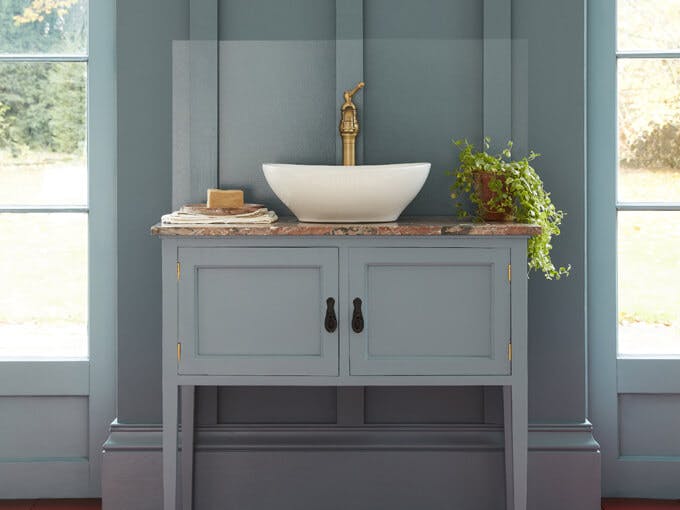 loakroom painted in muted blue shade 'Etruria' with a basin and round mirror in the center of two large windows.