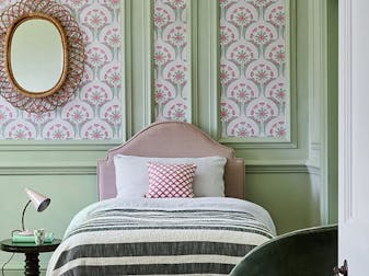 Bedroom with green wooden panelling, pink and green wallpaper, and a framed mirror on the walls.