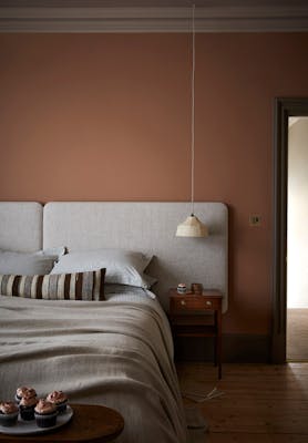 Bedroom painted in muted pink shade 'Split Pink' with a double bed next to a wooden sidetable.