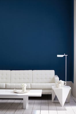 Living room painted in dark blue (Royal Navy) with a white sofa, lamp, table and wooden floor.