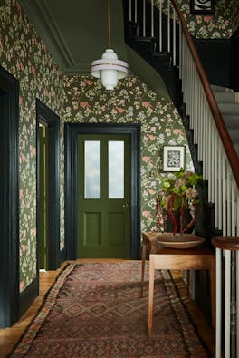 High ceiling hallway featuring dark green floral wallpaper (Aderyn - Olive Colour) with dark green woodwork and a tapestry rug.