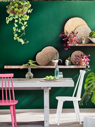 Outdoor dining space featuring a dark green (Puck) wall, a light grey (French Grey) table and a bright pink (Carmine) chair.