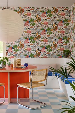 Breakfast room featuring multi-coloured wildlife print wallpaper (Animal Kingdom - Atomic Red) with a bright red table and wicker chairs next to a banquette.