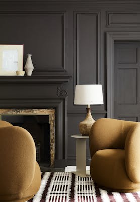 Deep brown paneled living space (Chocolate Colour) with contrasting dark yellow armchairs sat next to a fireplace and lamp.