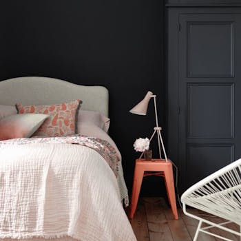 Bedroom painted in blue black 'Basalt' with a light pink bed and a contrasting bright orange stool.