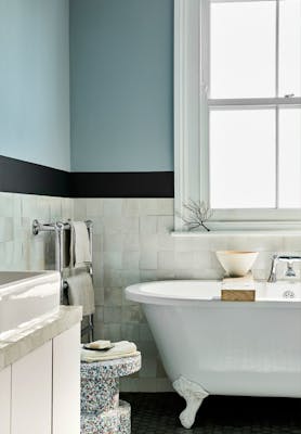 Bathroom with pale blue (Bone China Blue) upper walls and white tiles underneath, next to bathtub, window and sink.