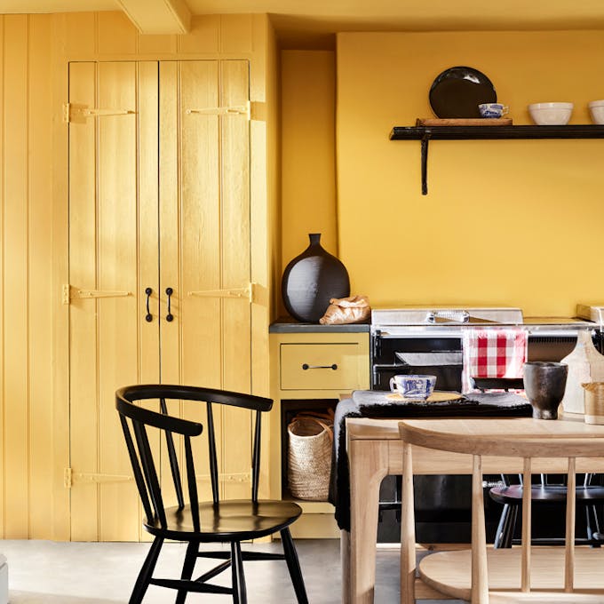 Kitchen color drenched in vibrant yellow shade 'Giallo', with a wooden table and chairs.