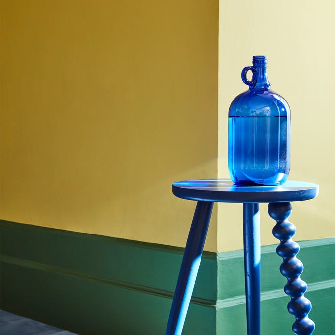 Dining room with vibrant yellow walls (Indian Yellow) with a green baseboard and bright blue stool.