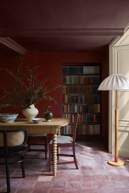 Dining room painted in cherry red shade 'Bronze Red' with a crimson ceiling (Arras) above wooden dining furniture and a book shelf.