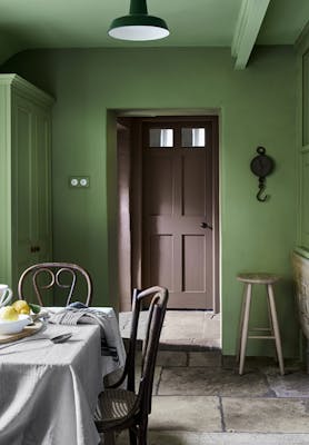 Deep green (Garden) dining space with contrasting brown door and a dining room table with chairs.