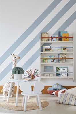 Child's reading corner painted in white (Shirting) with pale blue (Bone China Blue) diagonal stripes with a book shelf on the wall and a stuffed giraffe, table and chair.