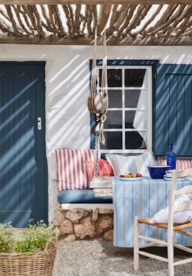 Yard with door and shutters painted in deep blue (Hicks' Blue) and a white wall, with a seating area and striped cushions.