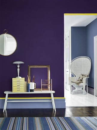 Hallway painted in dark purple blue shade 'Thai Sapphire' with a sidetable and stripy blue rug, with view into a drawing room painted in light blue 'Pale Lupin'.