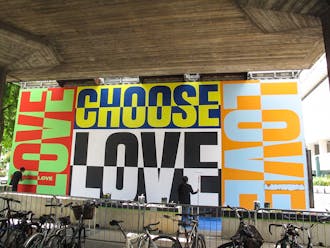 Brightly colored painted mural featuring the words 'Choose Love' with two women adding final touches with paint brushes.