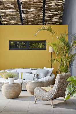 Outside seating area with a large wicker sofa and chair with a bright yellow wall (Yellow-Pink).