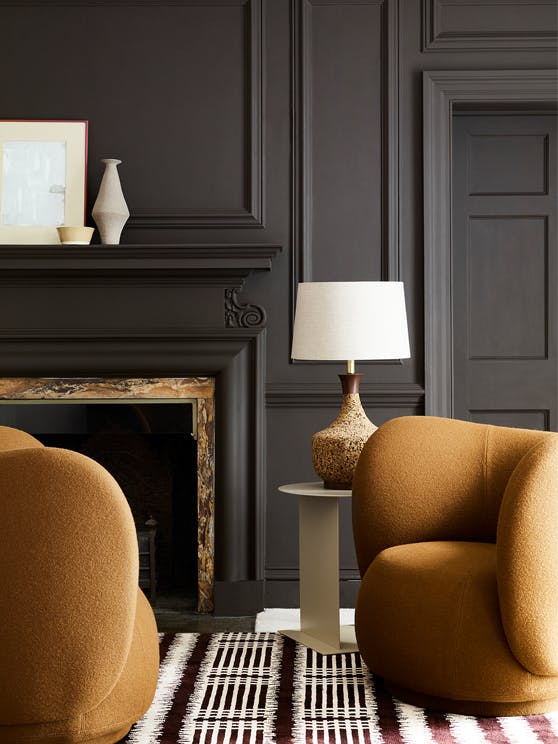 Deep brown paneled living space (Chocolate Colour) with contrasting dark yellow armchairs sat next to a fireplace and lamp.