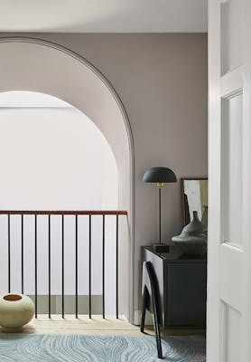 Hallway area painted in different shades of warm neutral China Clay under a large arch with a side table and bannister.