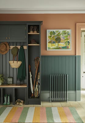 Paneled boot room with the top half painted in 'Split Pink' and the lower wall in 'Harley Green' with a cupboard to the left and a multi-colored stripy rug.