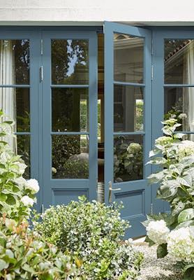 Back door painted in rich blue 'Air Force Blue' looking into a house, with plants and trees surrounding.