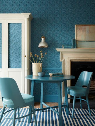 Dining space with a tonal blue wallpaper (Hoja - Air Force Blue) and white (Shirting) cupboard with blue table and chairs.